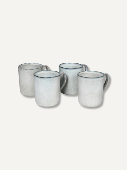 Four ceramic mugs with a speckled off-white glaze and a thin dark blue rim, arranged on a light beige background.