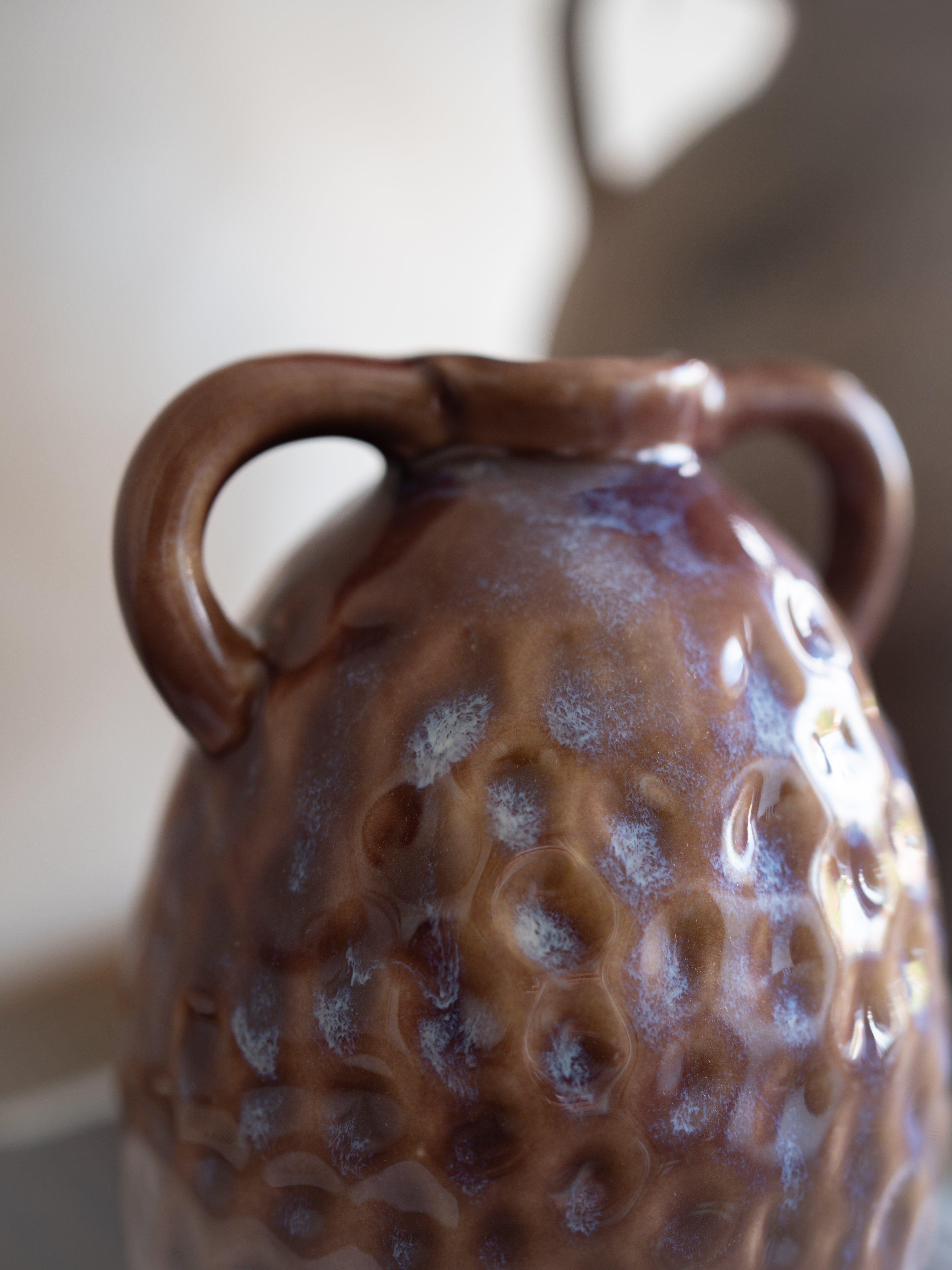 Close-up of a textured ceramic vase with two handles on a blurred background