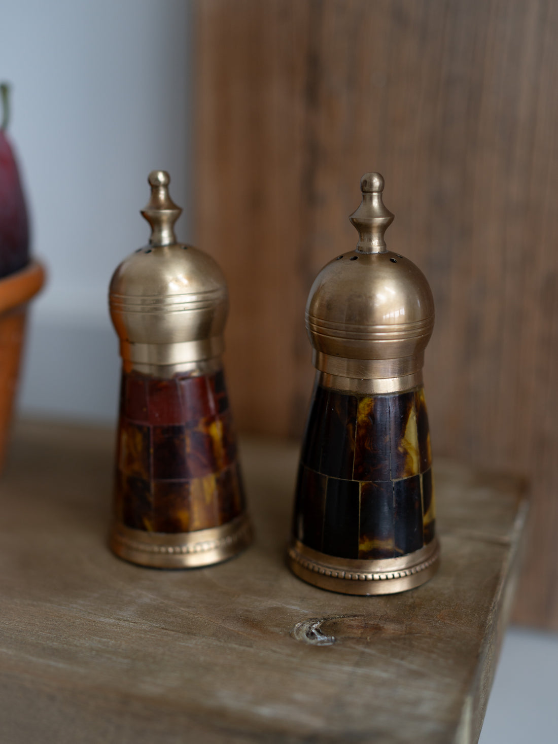 Two decorative salt and pepper shakers with tortoiseshell and brass design on a wooden surface.