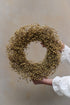 A person holding a round wreath made of natural dried flax.