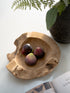 Wooden bowl with figs on a white surface with a plant in the background