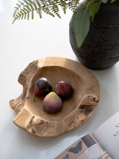Wooden bowl with figs on a white surface with a plant and book in the background