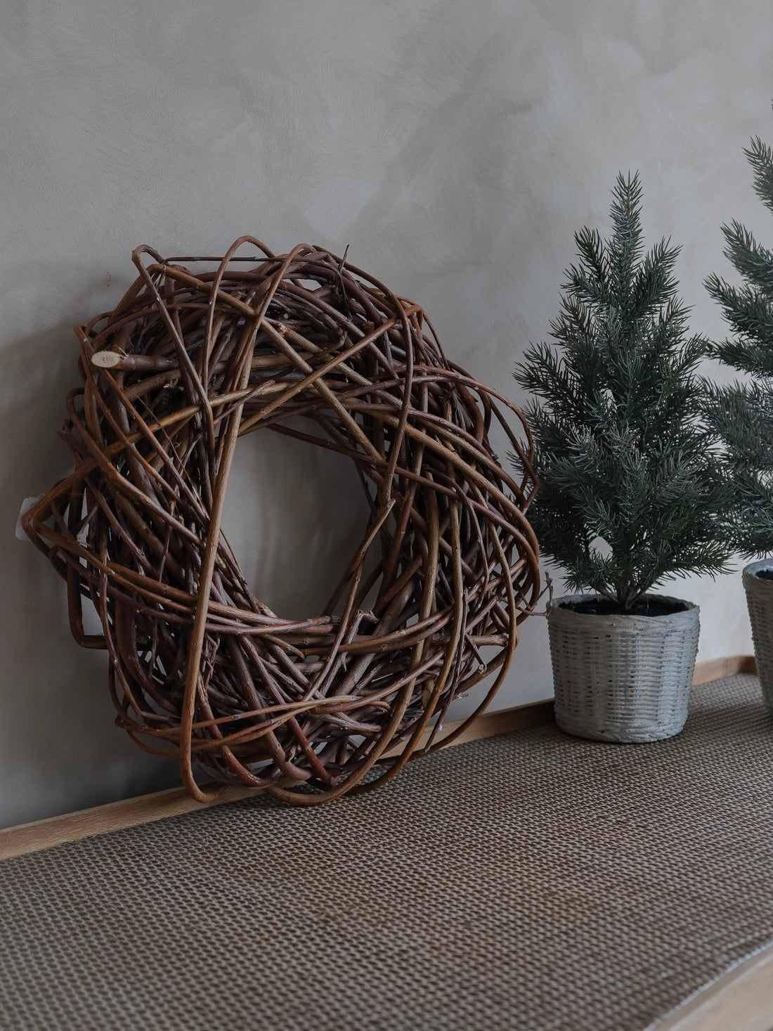 Woven decorative wreath and potted plants against a neutral wall.