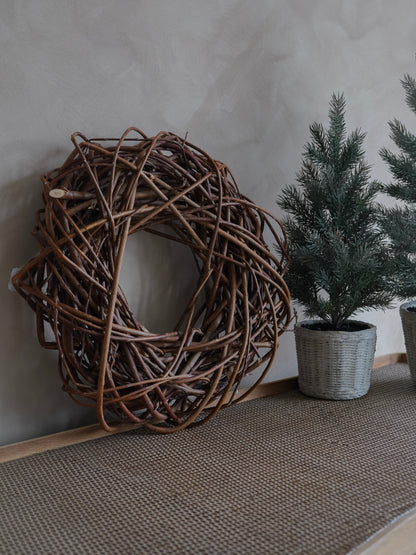 Woven decorative wreath and potted plants against a neutral wall.