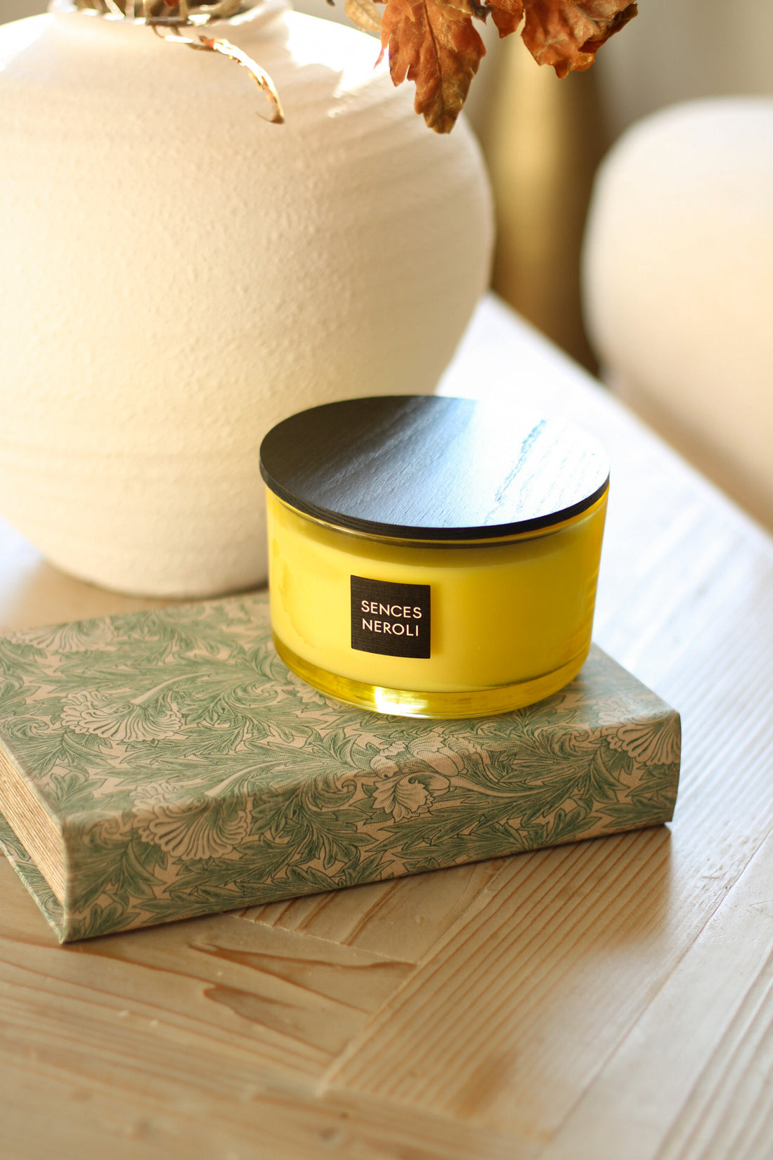 Neroli yellow candle with black lid on a decorative box, placed on a wooden surface.