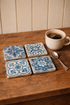 Ceramic coasters with blue floral patterns on a wooden surface next to a cup of coffee and spoon.