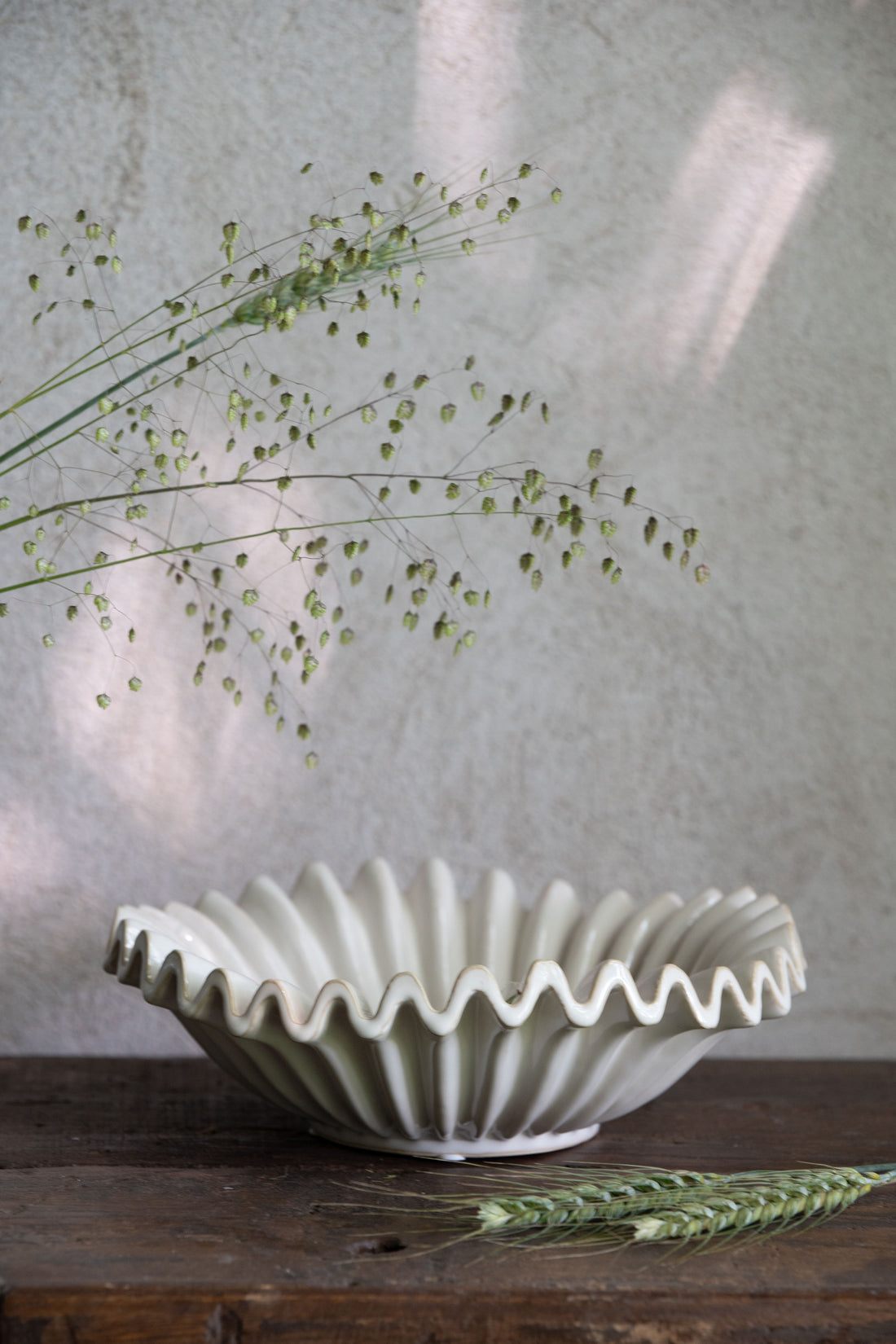 White ceramic bowl with wavy edge on a wooden surface with greenery.
