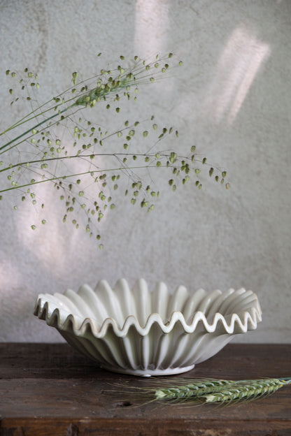 White ceramic bowl with wavy edge on a wooden surface with greenery.
