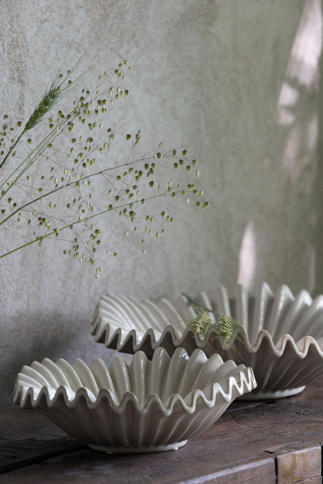 Three ceramic bowls with wavy edges on a wooden surface against a textured wall.