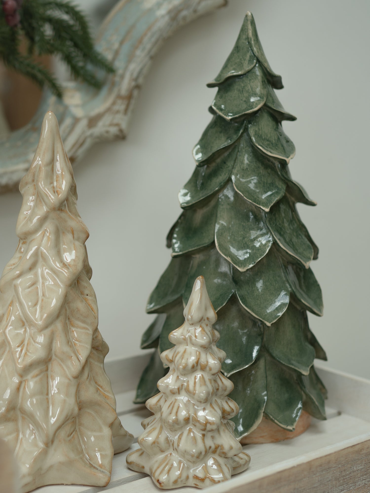Three ceramic Christmas tree ornaments in different sizes, including two in glossy cream and one in textured dark green, displayed on a white tray.