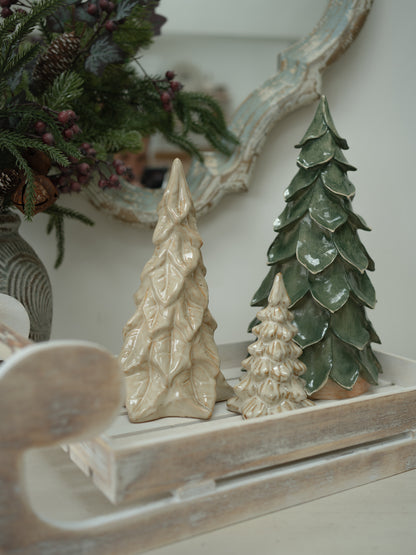 Three textured ceramic Christmas tree ornaments in cream and green glazes displayed on a rustic white wooden tray.