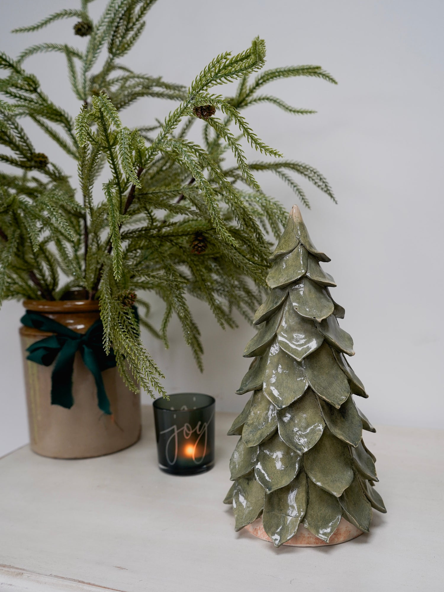 Decorative ceramic Christmas tree with a candle and potted plant on a white surface.