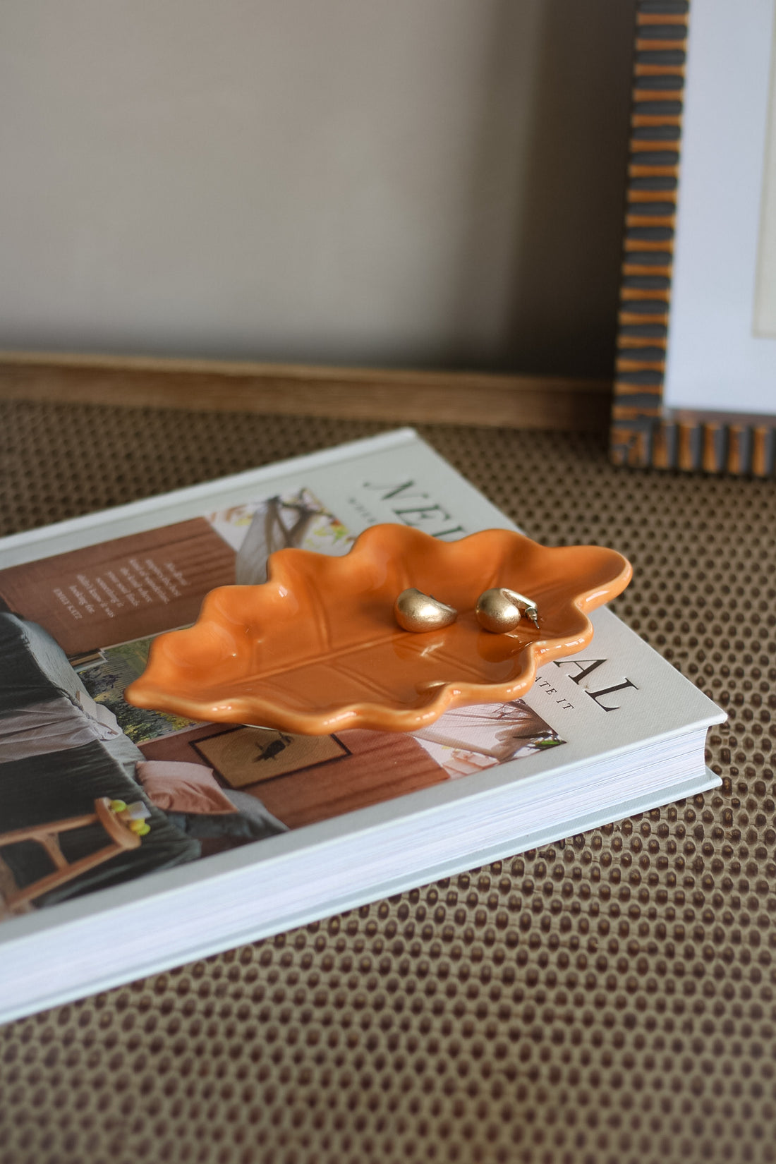 Orange leaf trinket dish with gold earrings on a book