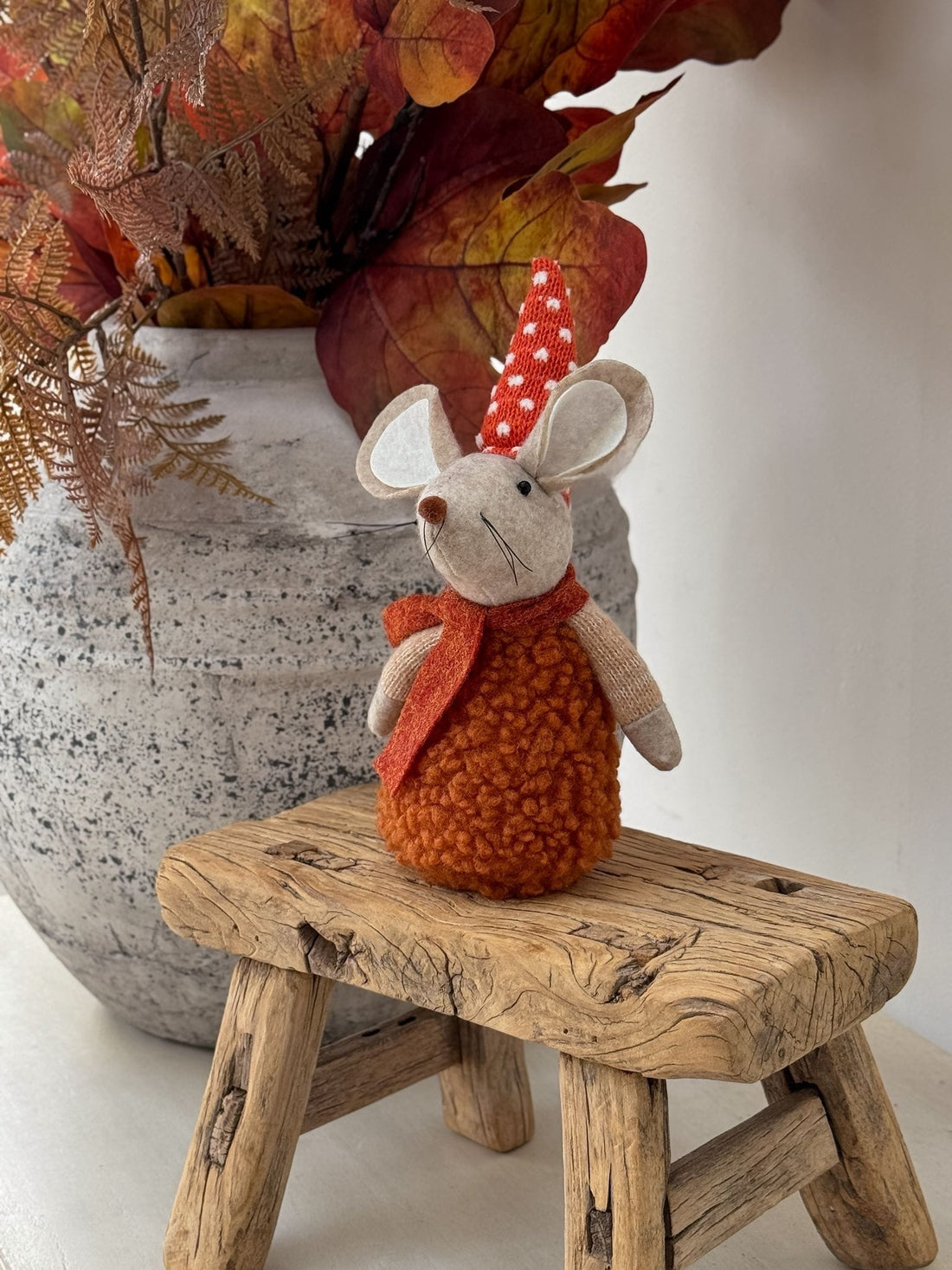 Small orange mouse with a red bow tie on a wooden stool with autumn leaves in the background