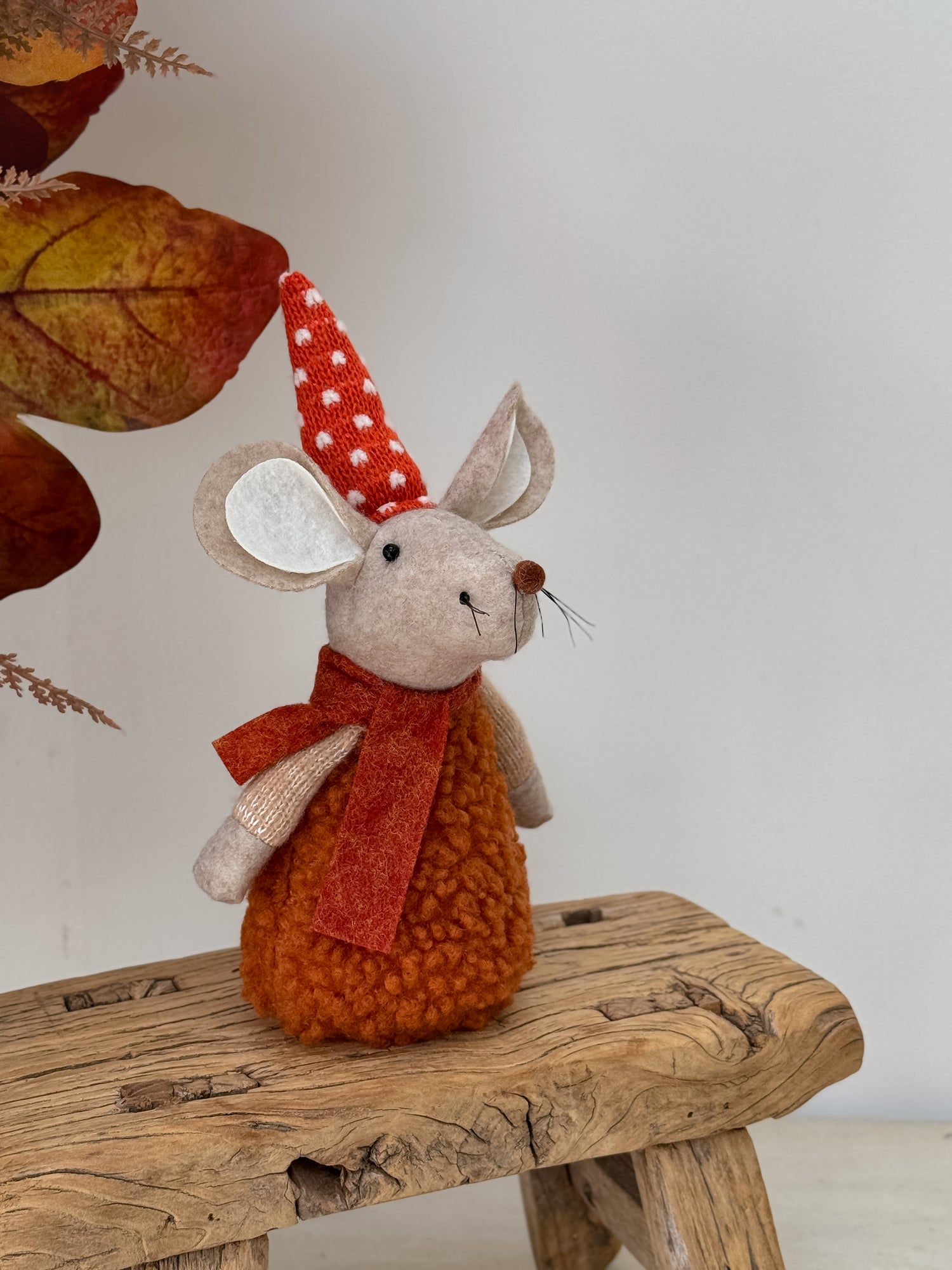 Autumn mouse decoration with a red scarf and hat on a wooden surface with autumn leaves.