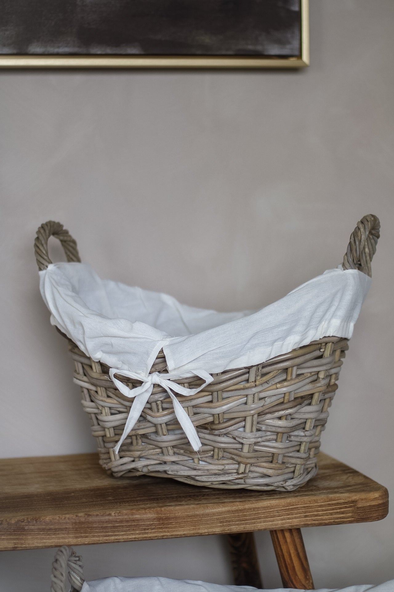Wicker laundry basket with white liner on a wooden surface against a plain wall.