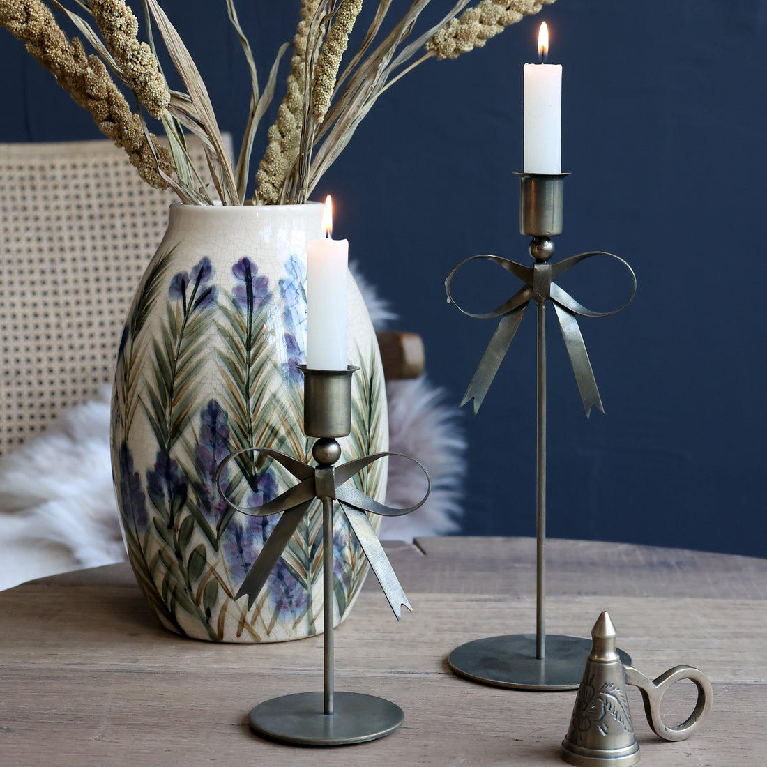 Decorative bow candle holders and a vase with dried plants on a wooden surface.