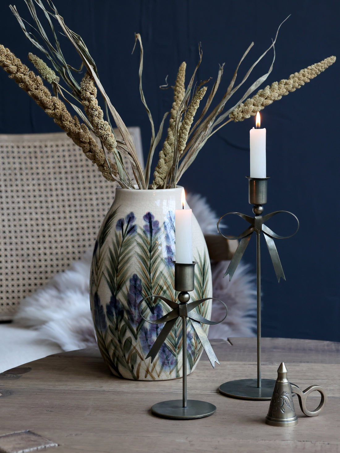 Decorative elements including a vase with dried plants, bow candlesticks, and a metal candle holder on a wooden surface