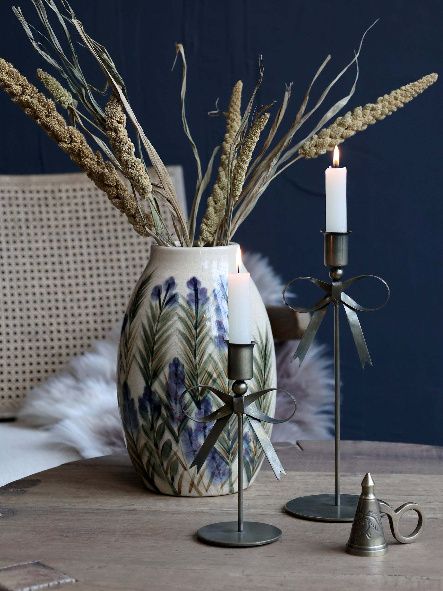 Decorative elements including a vase with dried plants, bow candlesticks, and a metal candle holder on a wooden surface