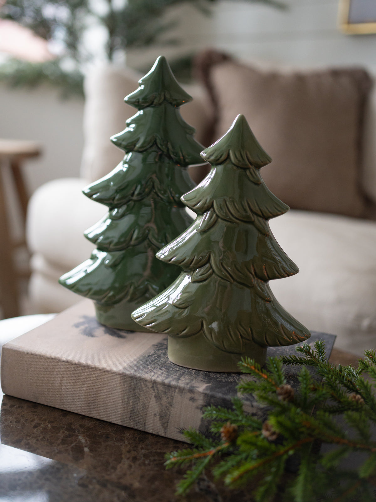 Pair of Moss Green Ceramic Christmas Trees on book storage box with faux branch in the foreground