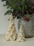 Two ceramic Christmas tree ornaments in cream and off-white glaze, displayed next to a rustic gray patterned vase filled with evergreen branches and pinecones.