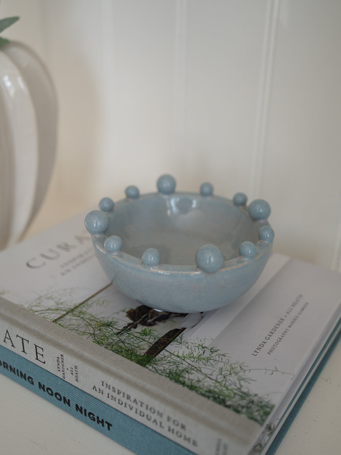 Decorative pale blue ceramic bowl with spherical design on top of books