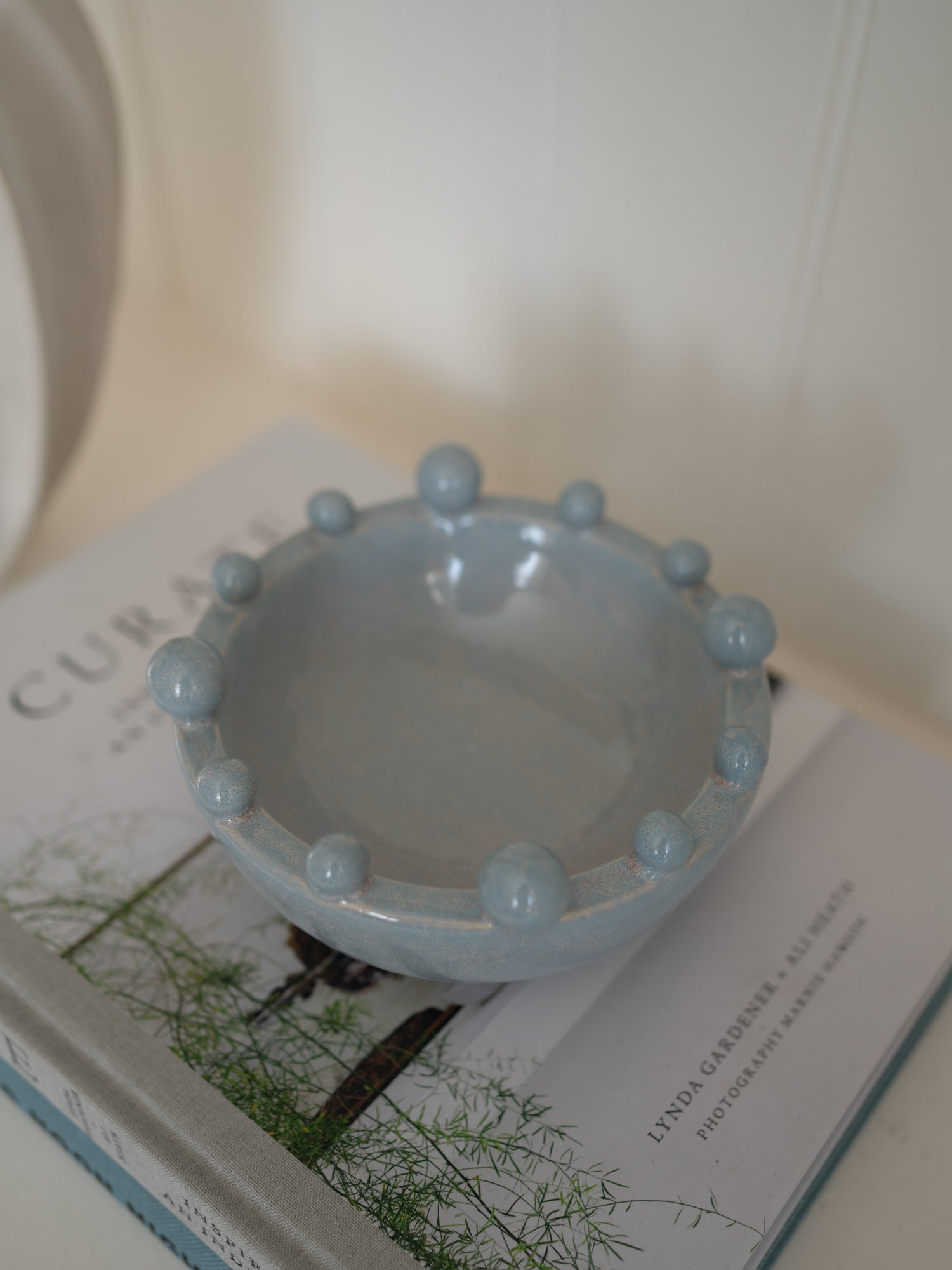 Light blue ceramic decorative bobble bowl on a book with a blurred background