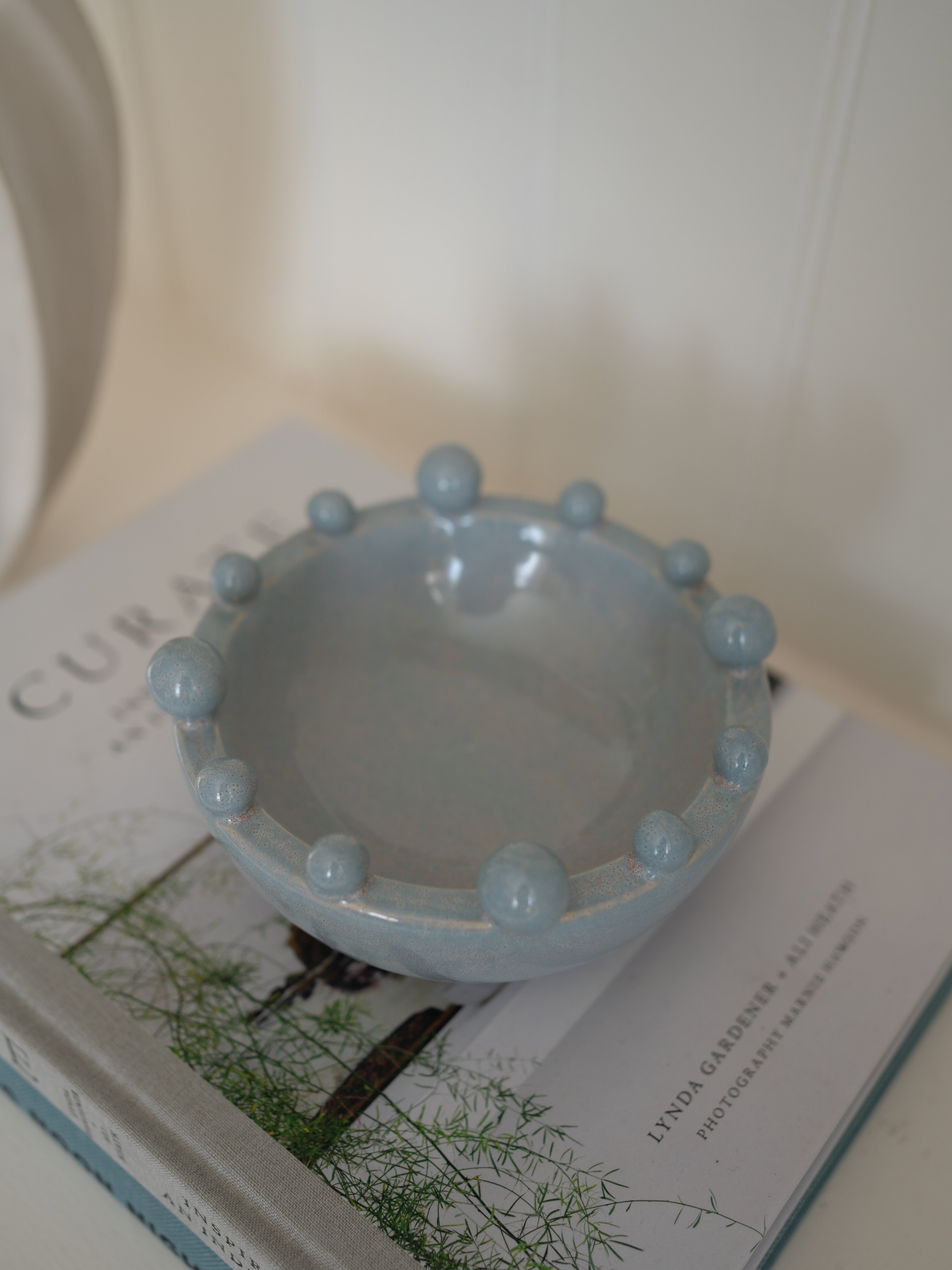 Light blue ceramic decorative bobble bowl on a book with a blurred background