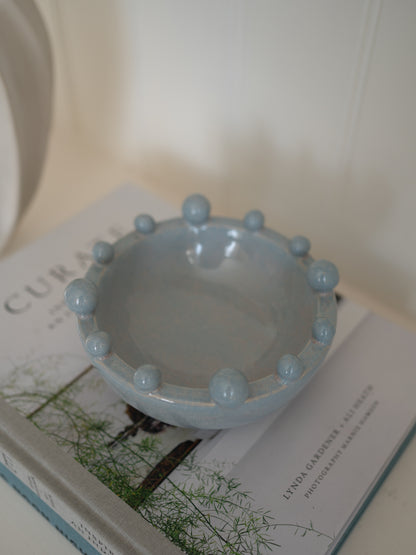 Light blue ceramic decorative bobble bowl on a book with a blurred background