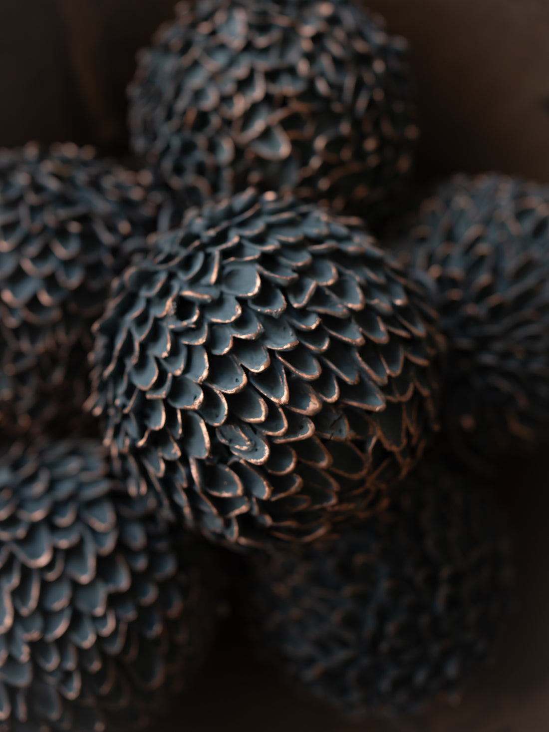 A close-up of several dark, textured decorative spheres with a pine cone pattern, photographed in low light against a dark background.