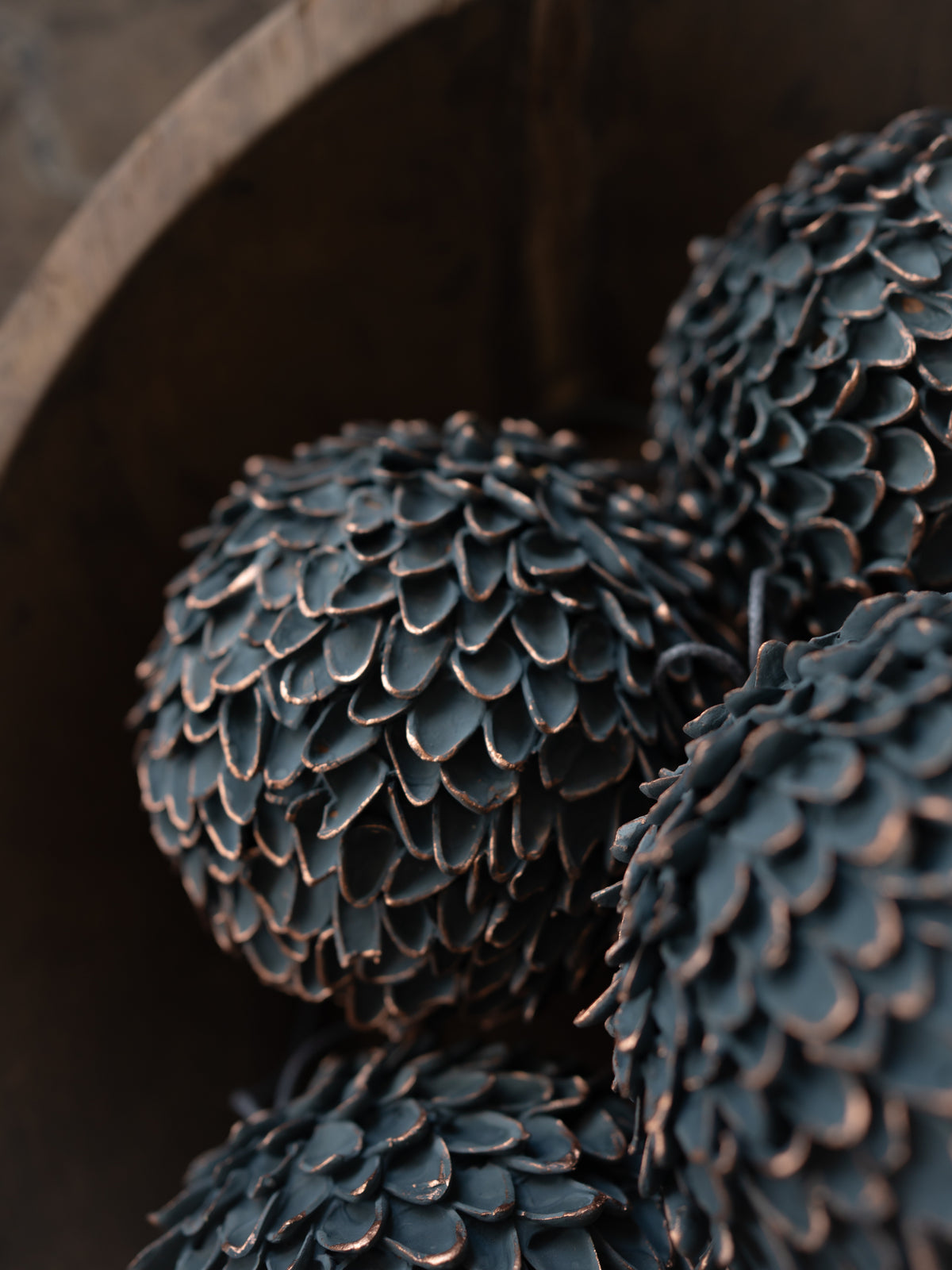 Close-up of a decorative sculptural object with a dark brown and charcoal, pine cone-like textured surface, resting inside a dark wooden bowl.