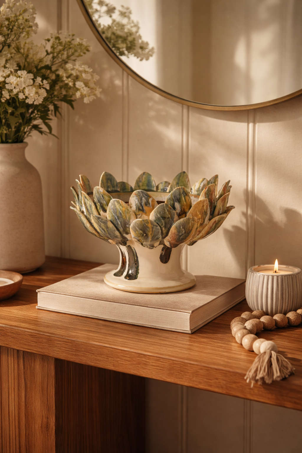 Decorative artichoke-shaped bowl on a wooden surface with a vase and candle in the background.