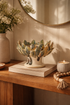 Decorative artichoke-shaped bowl on a wooden surface with a vase and candle in the background.