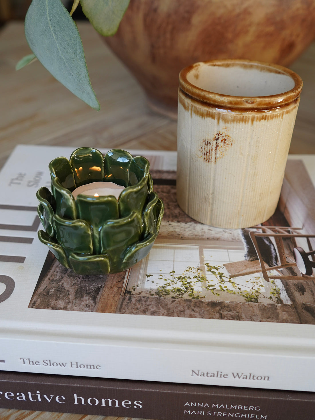 Green ceramic candle holder on a book with a wooden object in the background