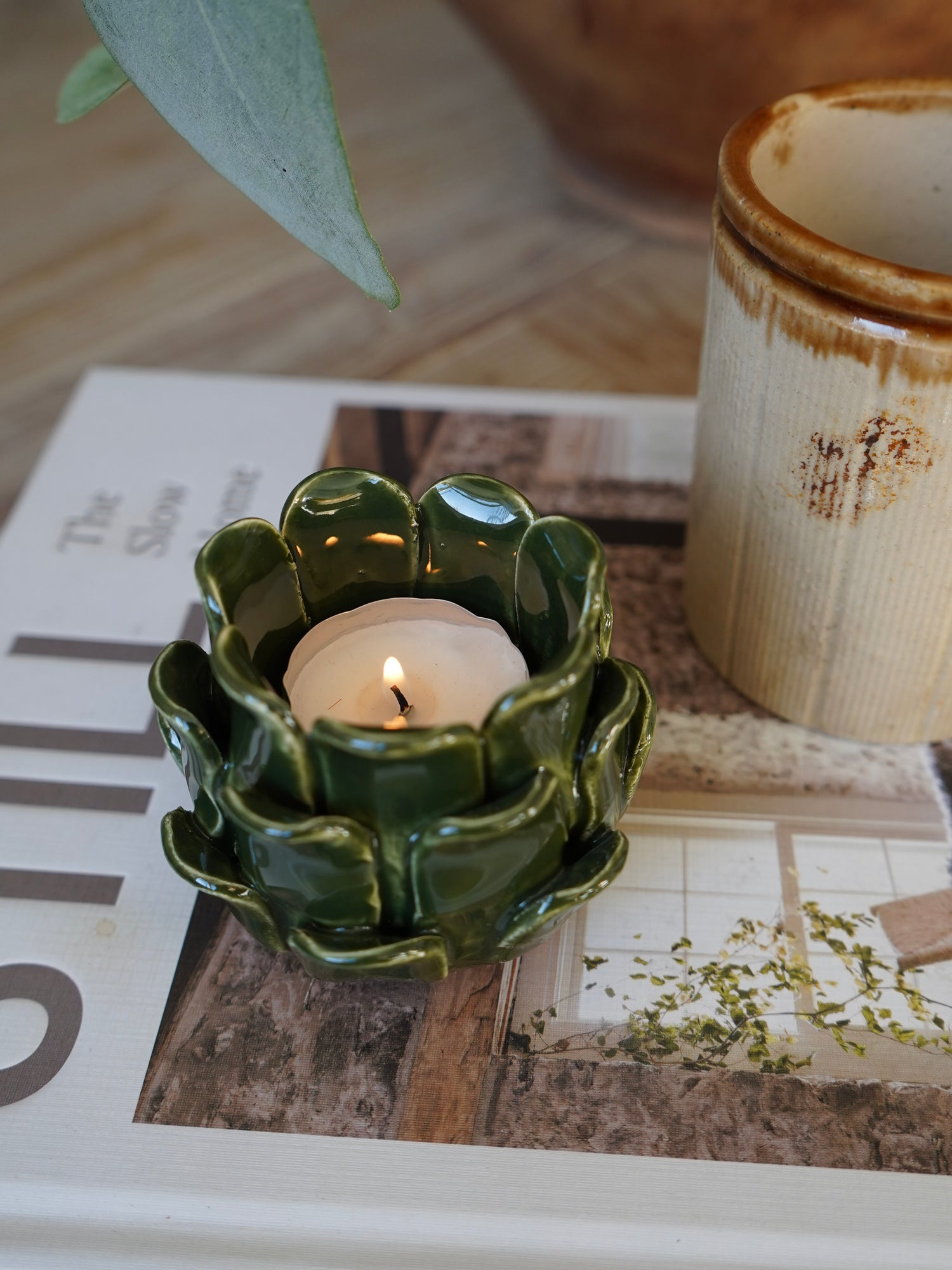 Green ceramic candle holder with a lit candle on a newspaper