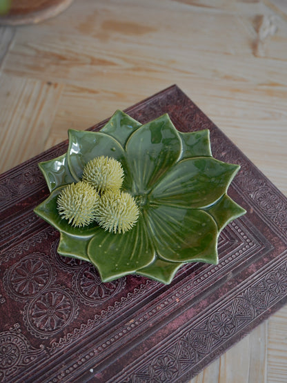 Green ceramic flower-shaped trinket dish with decorative elements on a textured surface