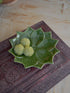 Green ceramic flower-shaped trinket dish with decorative elements on a textured surface