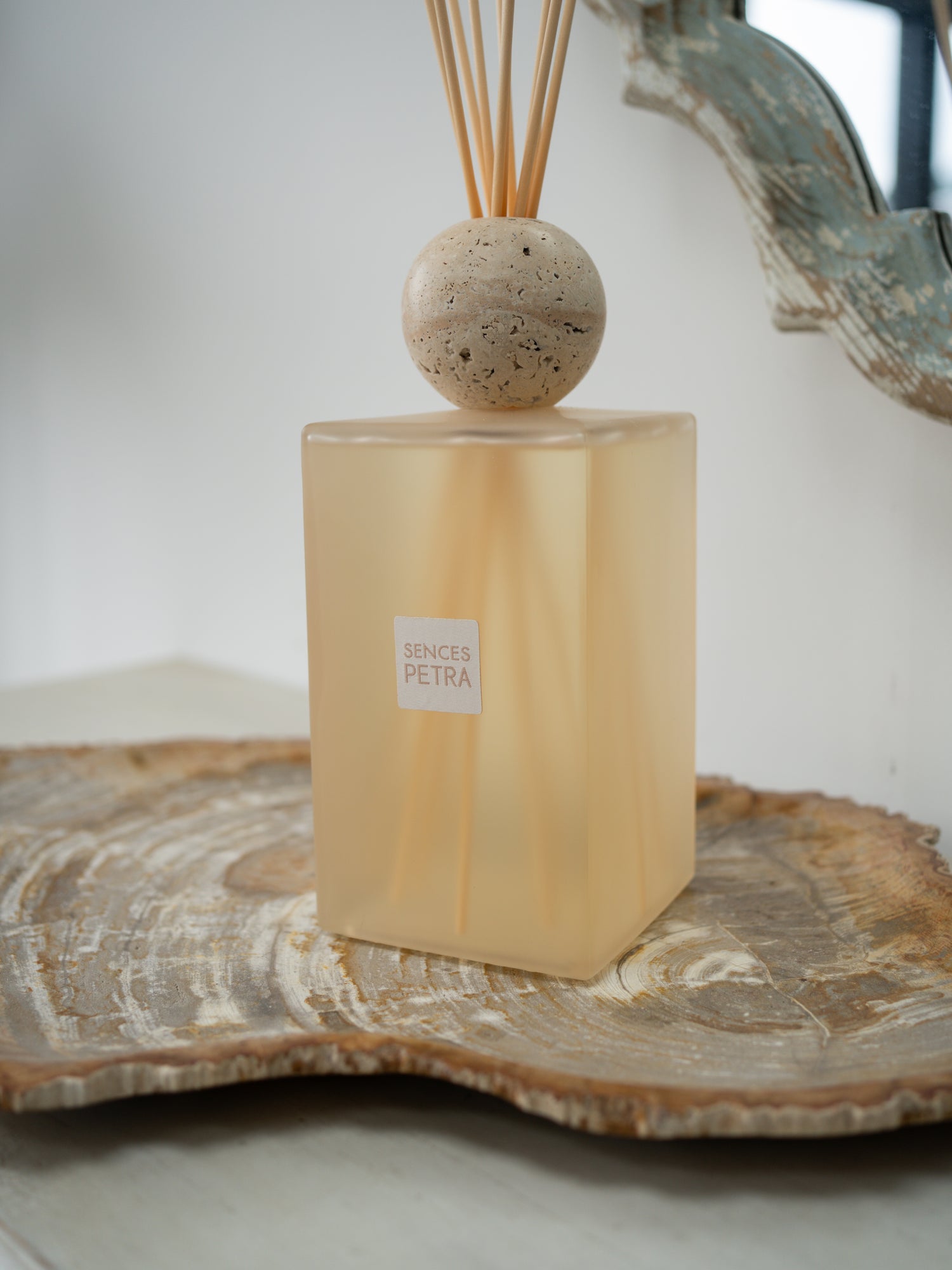A extra large petra reed diffuser bottle in frosted warm beige glass with a round stone top and natural reed sticks, displayed on a wood slice tray against a soft neutral background.