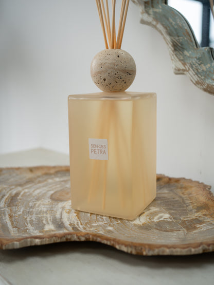 A extra large petra reed diffuser bottle in frosted warm beige glass with a round stone top and natural reed sticks, displayed on a wood slice tray against a soft neutral background.