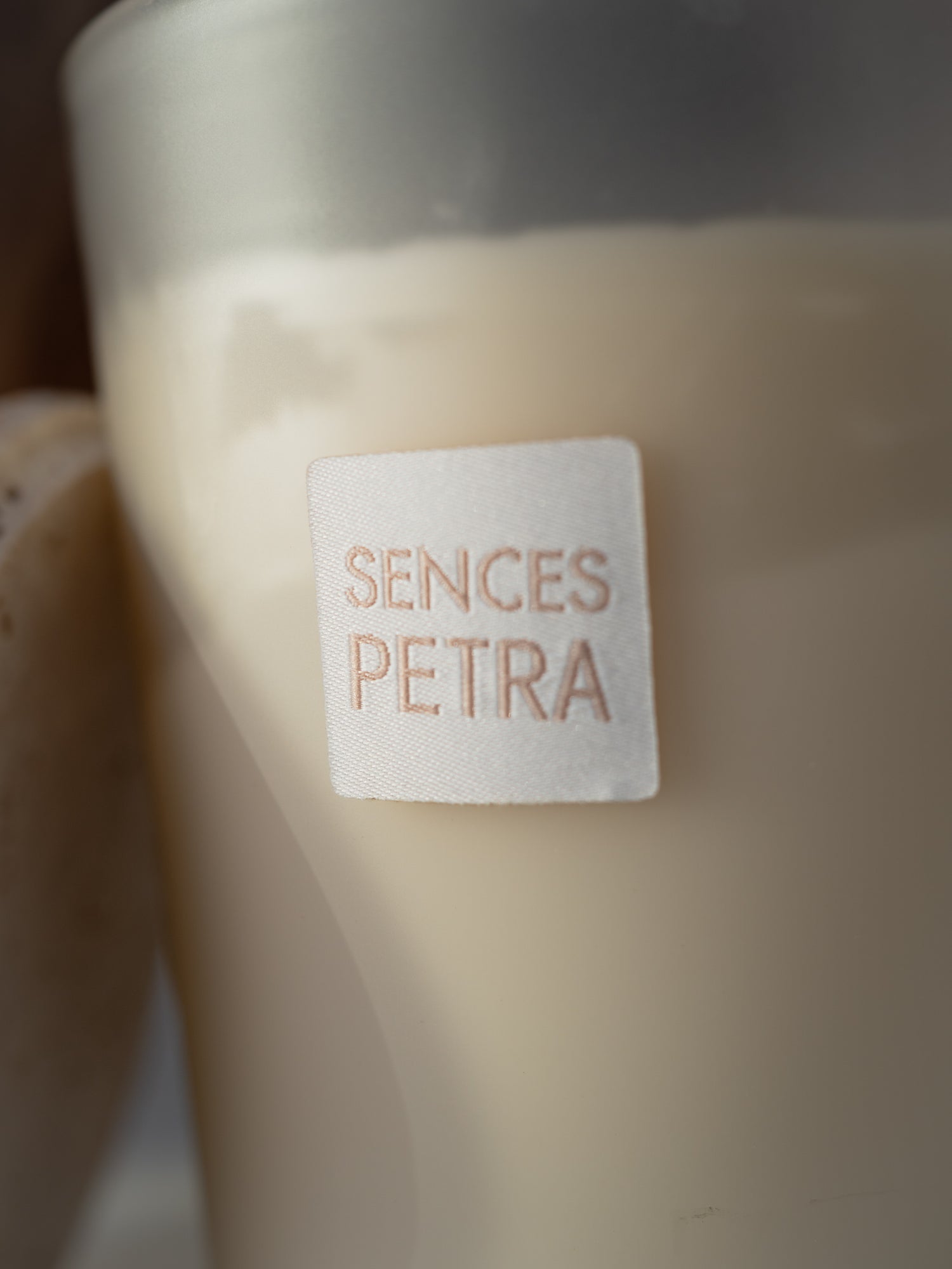 A close-up of a candle in a frosted glass container with a cream-colored wax and a white square label that reads &