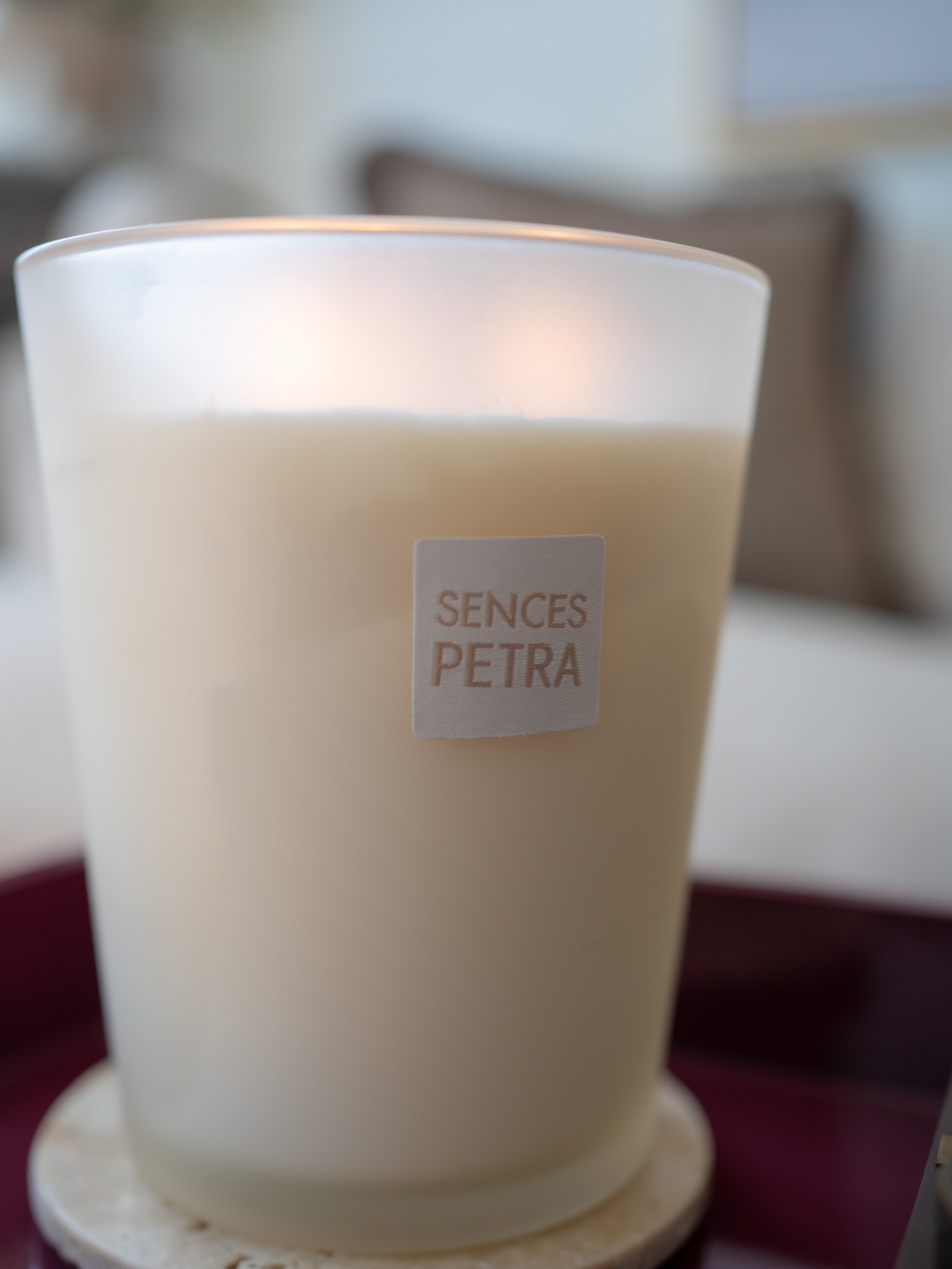 A frosted glass candle jar with a cream-colored wax inside, featuring a square white label that reads &