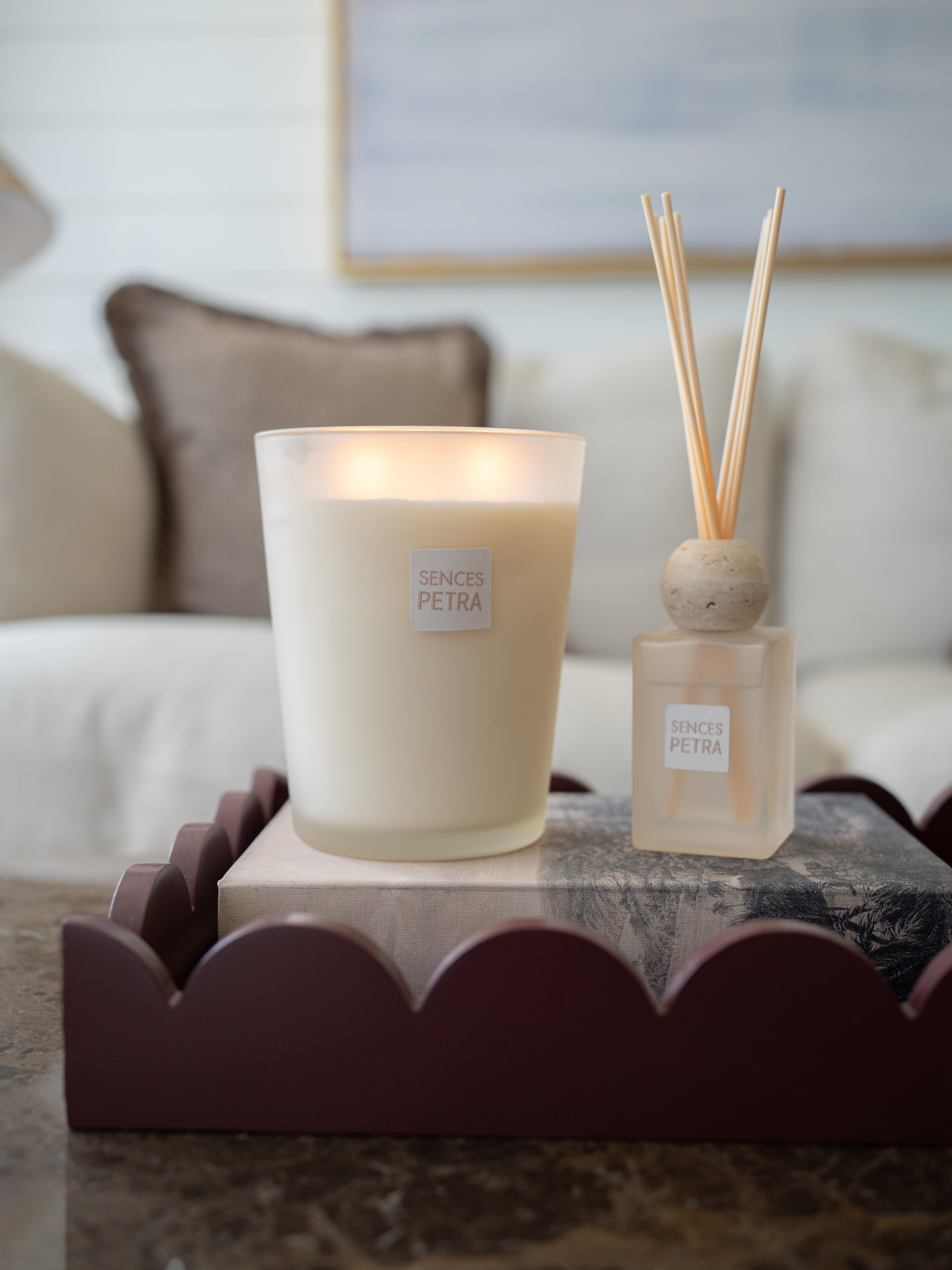 A lit frosted glass candle and a matching reed diffuser bottle with wooden reeds, both labeled &