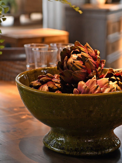 Decorative green bowl with faux artichokes on a wooden surface