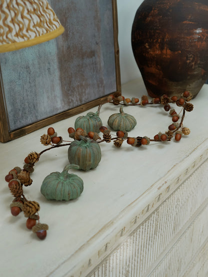 Decorative wreath with small pumpkins and acorns on a white surface.