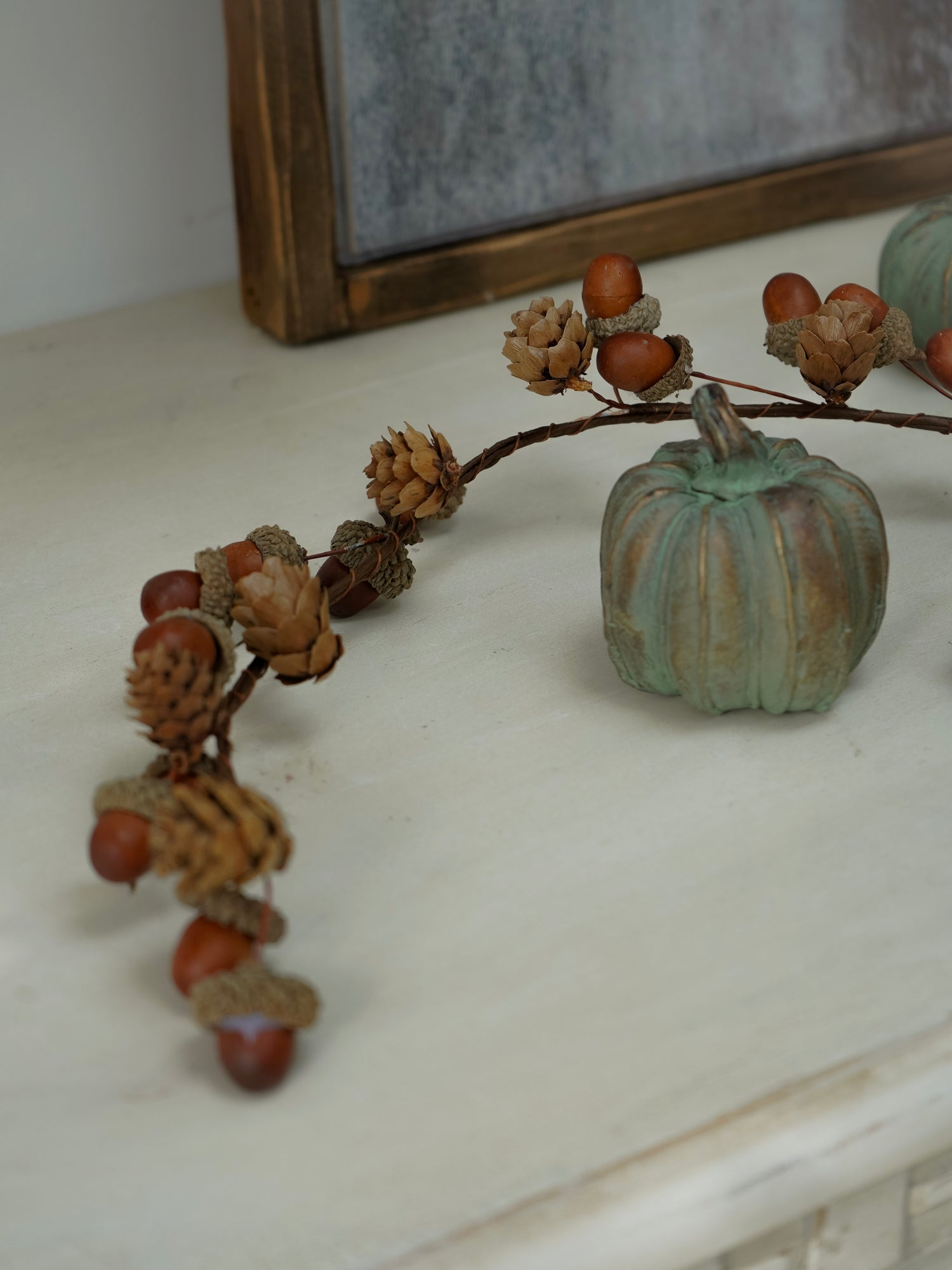 Decorative branch with acorns and a small pumpkin on a white surface.