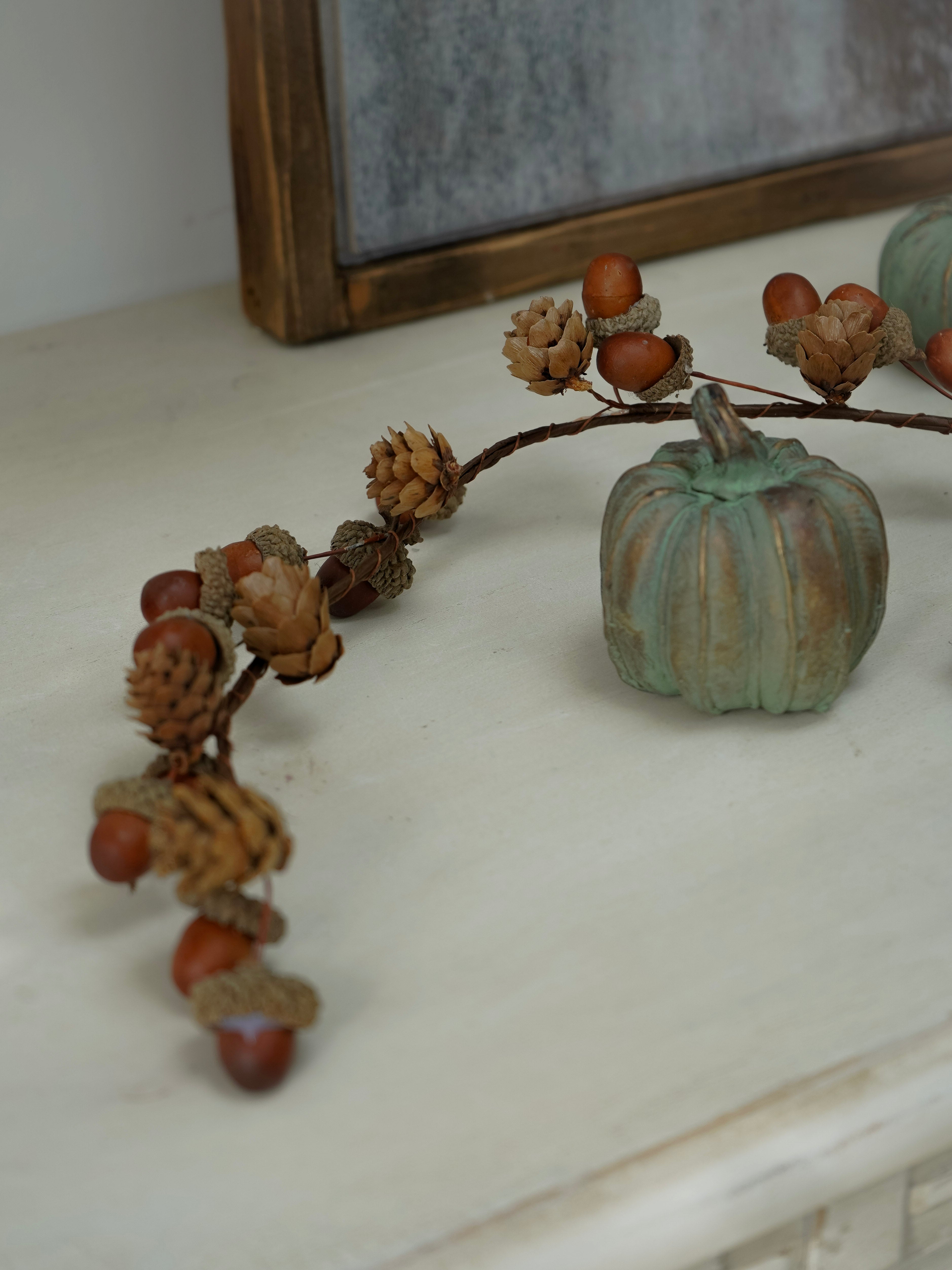 Decorative branch with acorns and a small pumpkin on a white surface.