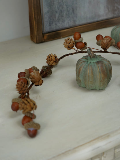 Decorative branch with acorns and a small pumpkin on a white surface.