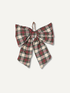 A large fabric bow in a red, green, and cream plaid pattern, featuring a small brown leather loop at the top, shown against a light off-white background.