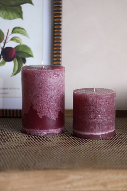 Two plum candles on a textured surface with a blurred background