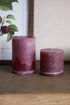 Two plum candles on a textured surface with a blurred background